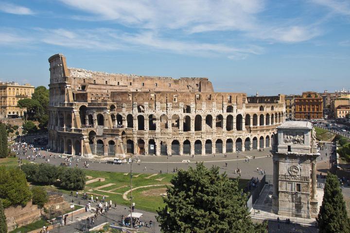 a castle with a clock on the tower of the city with Colosseum in the background